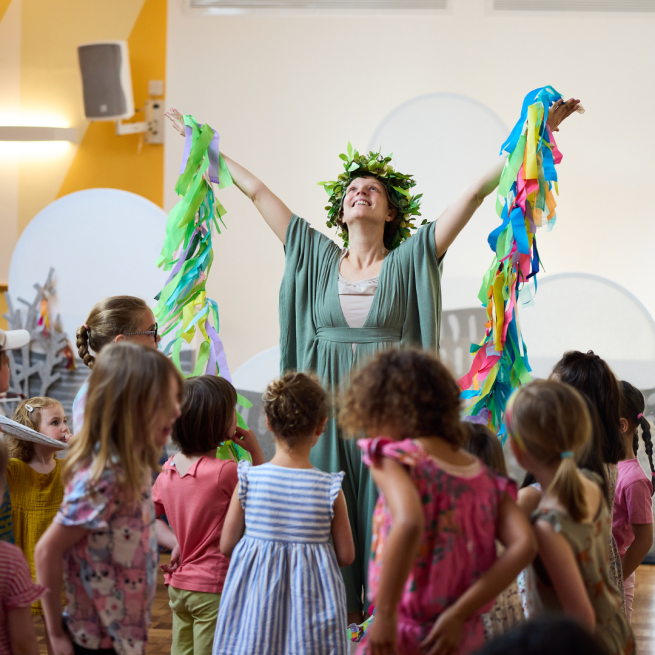 The mountain witch in her flower crown dances with the children in the audience