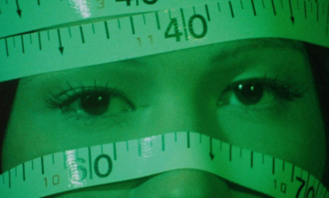 A close-up of a womans eyes with the rest of her face wrapped in measuring tape 