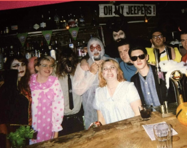 A group of people in spooky halloween fancy dress behind a bar.