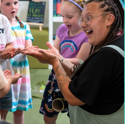 A photograph of Liv and some children opening their hands like a book and looking excited