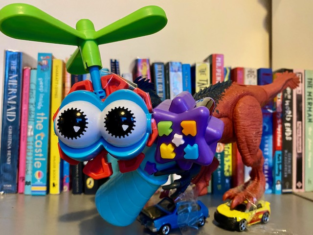 A robot made up of different parts of toys with books in the background