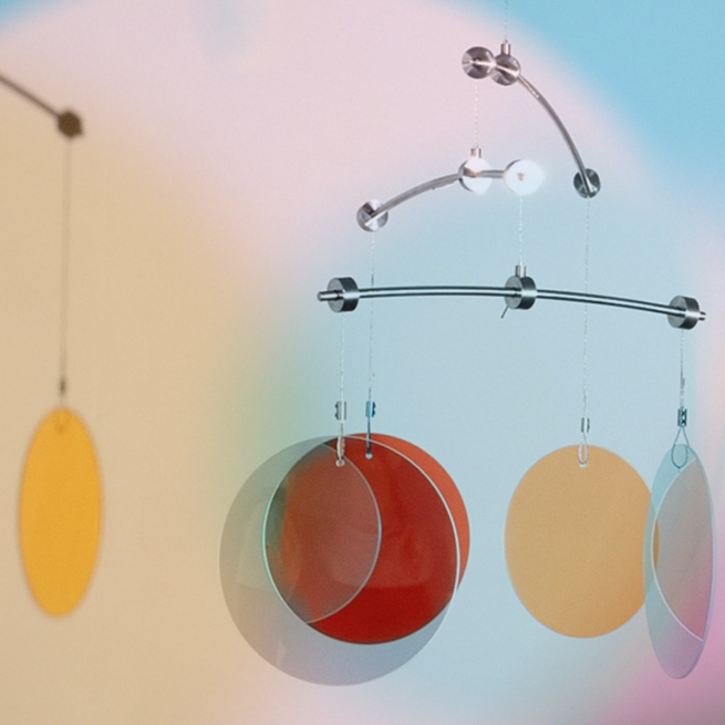 Coloured glass circle hang from the arms of a silver metal mobile reflecting pastel colours onto the white wall behind