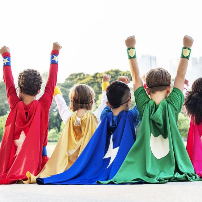 Four children sat wearing superhero capes with varying colours and symbols.