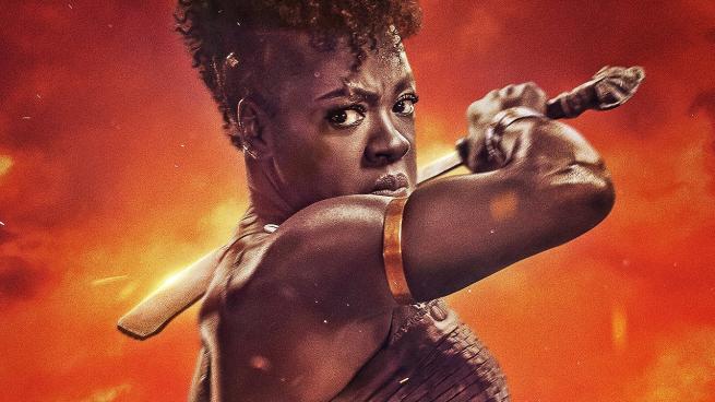 Viola Davis faces the camera with amachete in one hand, ready to slice it rowards the camera. The background is a firey orange. 