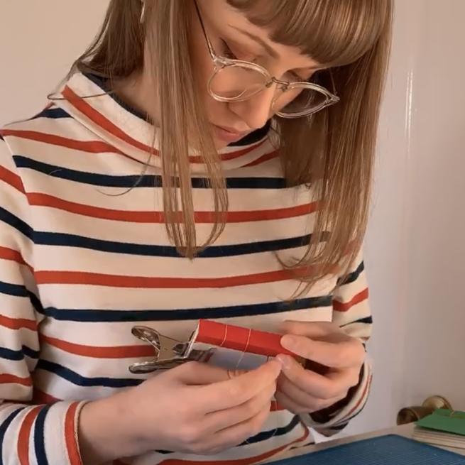 a photo of a lady wearing a blue and re striped top holding a sewing a booklet which she is holding in both hands.