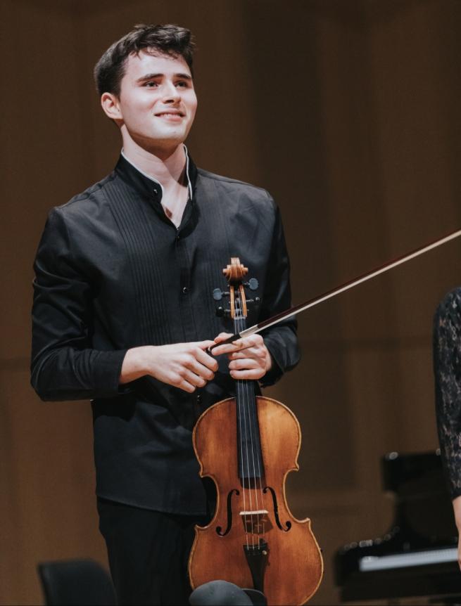 Soloist Jaren Ziegler smiling whilst holding his viola. 