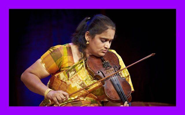 A woman wearing a yellow sari playing the violin.