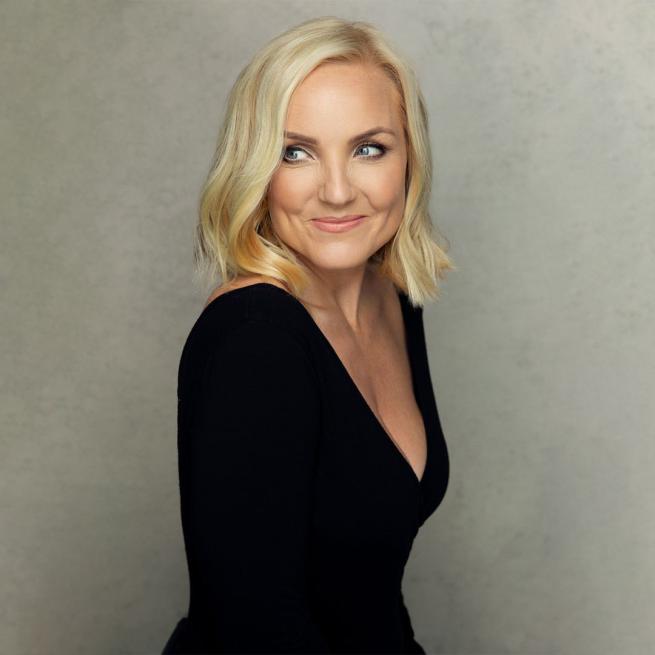 Kerry Ellis wearing a back top looking over her right shoulder.