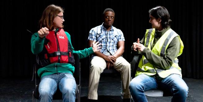 Three people on chairs on a theatre stage