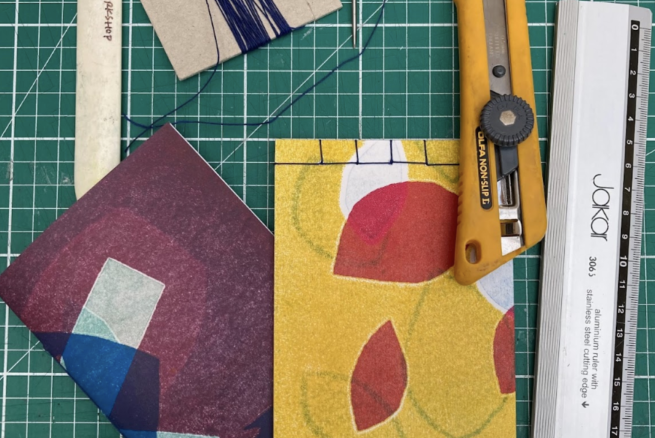 Multicoloured hand-bound books, with tools including a craft knife, thread and metal ruler.