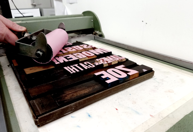 Pink ink being on rolloer being used to coat some wooden type reader to print from