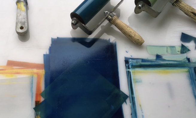 Blue, green and orange printmaking inks and rollers on a white acrylic board.