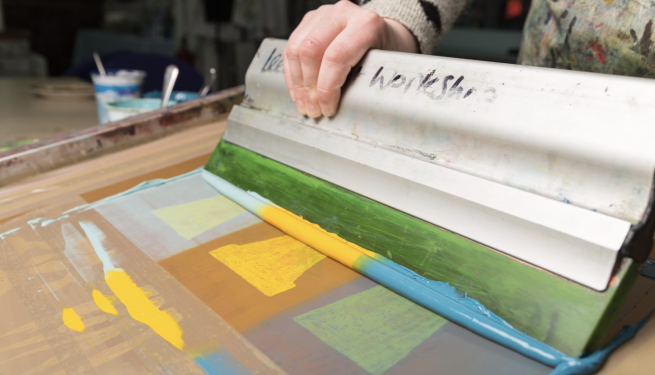 Blue and yellow inks being pulled through a screen creating an image of plant pots