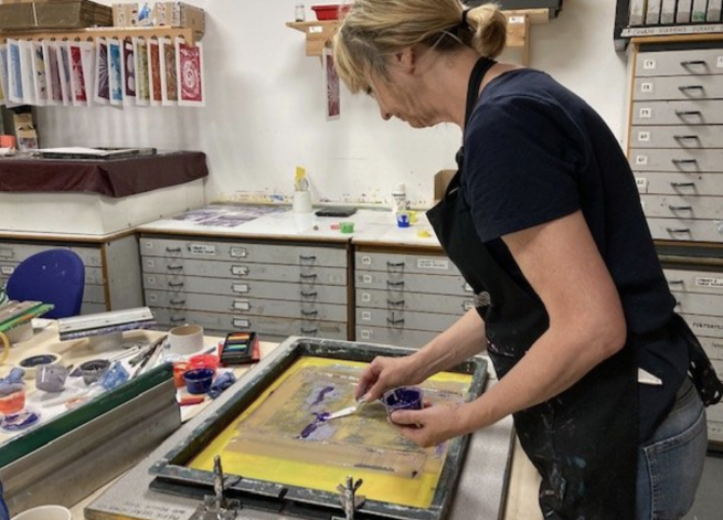 A woman adding purple ink to a screen ready to print from.