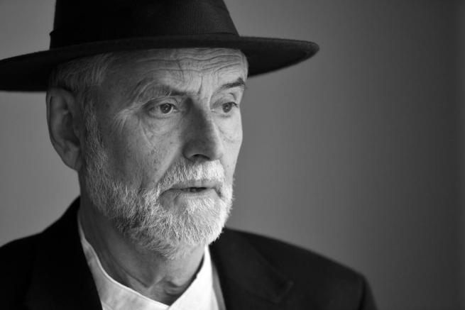 Black and white image of an older man looking off camera wearing a smart, black hat.