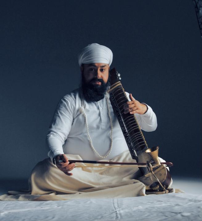 Man sitting down and holding an Esraj.