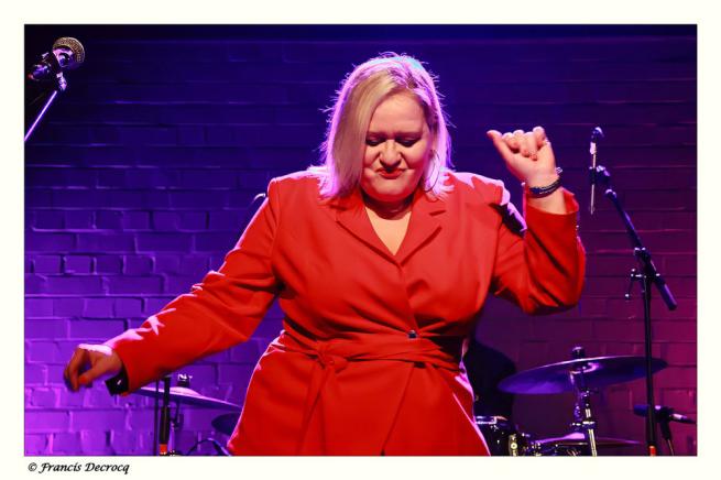 Emma Wilson appears in a pose on stage wearing a scarlet red outfit