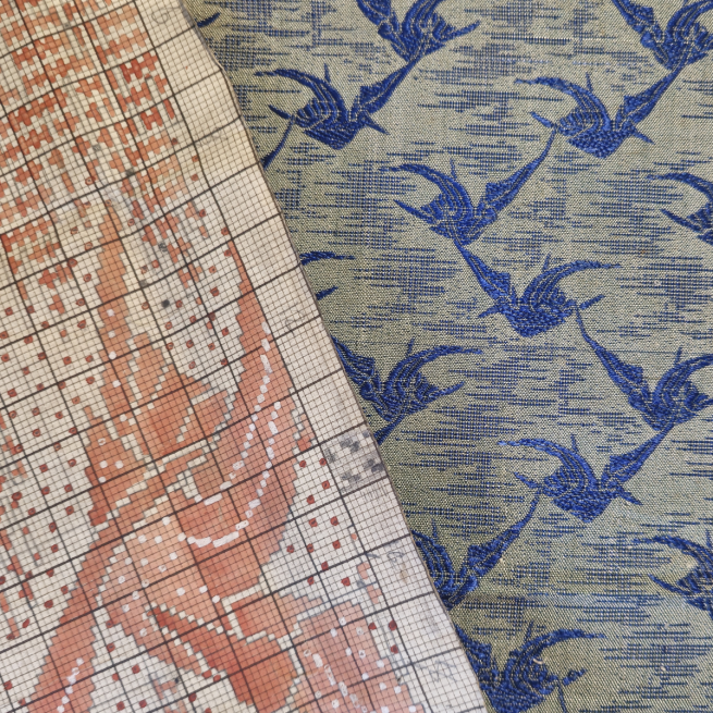 A textile pattern in pink on white graph paper, over a blue and white patterned fabric of birds