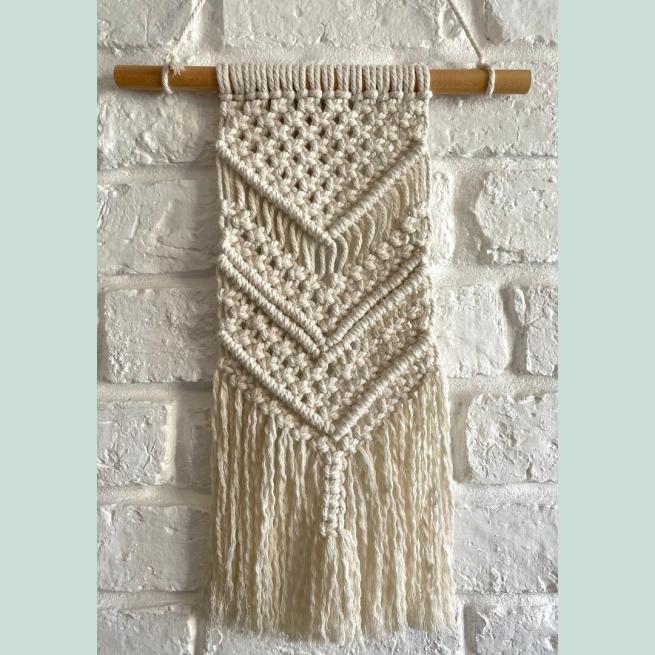 A beige macrame wall hanging against a white brick wall