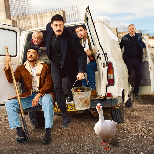 Four men hanging out the back of a white van, one holding a bucket and a goose is on the concrete floor just in front of the bucket. One man is hanging out the front right door.