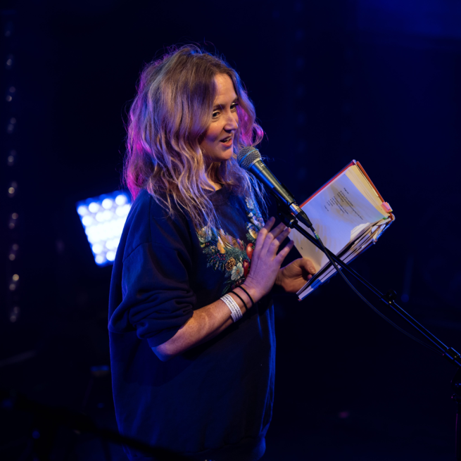 Poet Holly McNish performing on stage holding her book