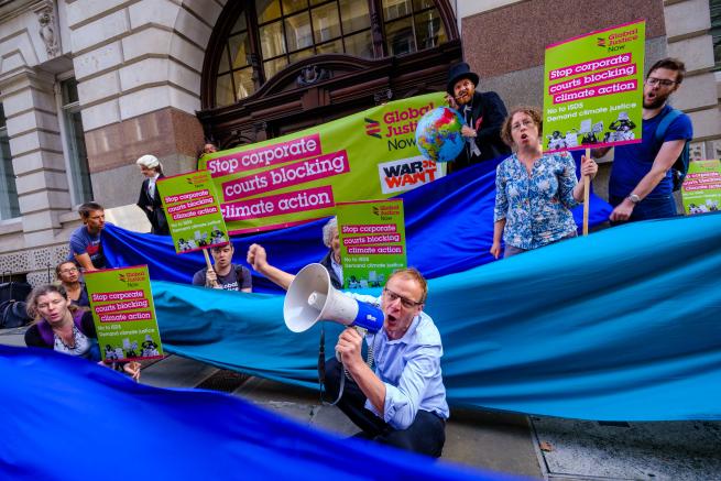 A group of demonstrators outside a court in London holding placards demanding that corporate courts stop blocking climate action 