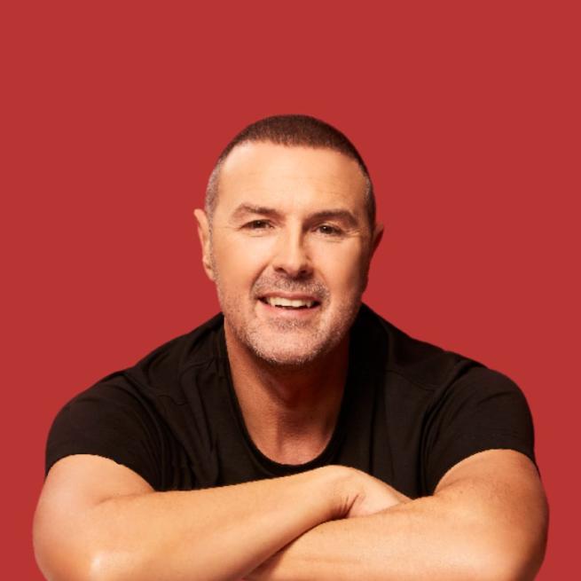 Paddy McGuinness smiling with a rusty red background.