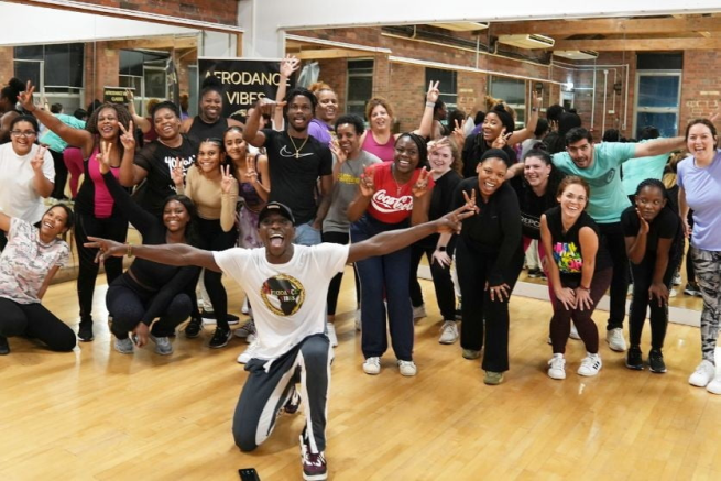 A group of people wave to the camera in a dance studio