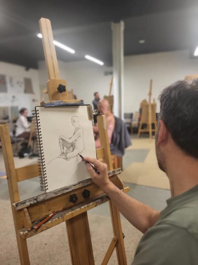 Point of view of an artist sat at his easel drawing a life model in pencil