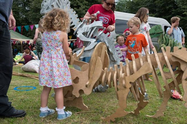 children outdoors with a wooden dinosaur fossil