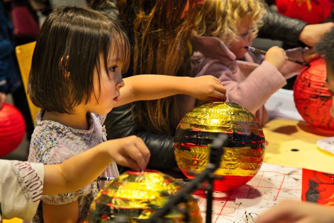 Children are painting Chinese lanterns with gold ink to mark the Lunar New Year