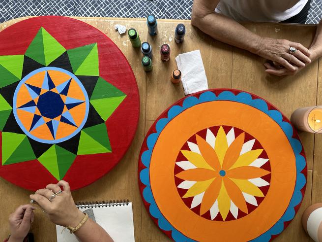 colourful, circular folk art Hex Signs are in view from above, being painted.