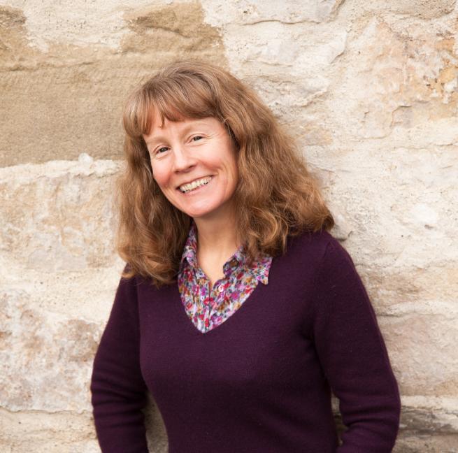 Picture of author Julia Chapman standing against a stone wall smiling at the camera 