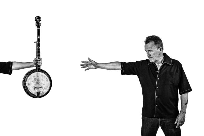 A man holding his arm out to the left reaching for a banjo being held in the air.