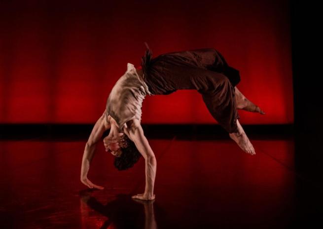 Dancer performing a backbend on stage with a red background.