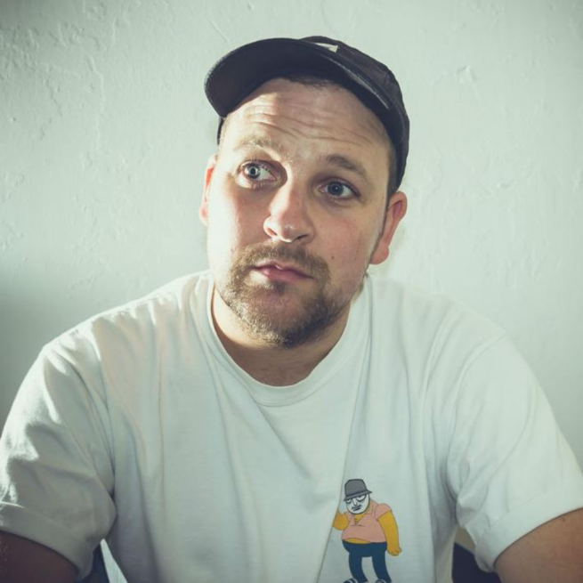 A photographic portrait of spoken word artist Polarbear wearing a baseball cap and white t-shirt.