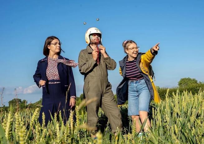 Three people stood in field pointing to the distance