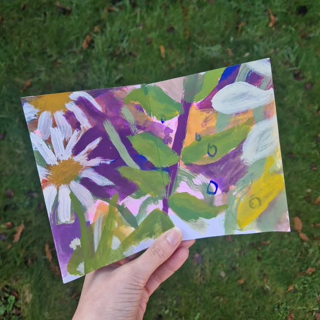 Colourful, hand-painted zine with florals and botanicals held over grass background