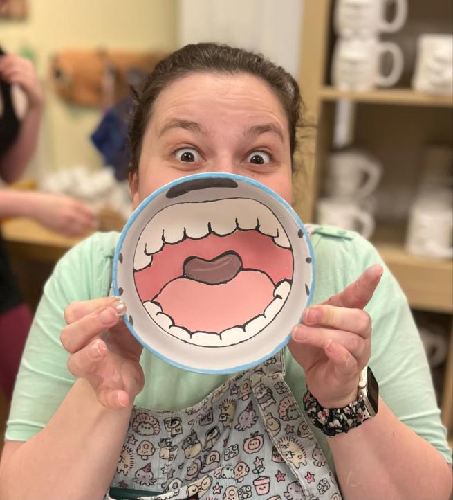 Photo shows a woman holding up a bowl which has a painting of a mouth on the inside