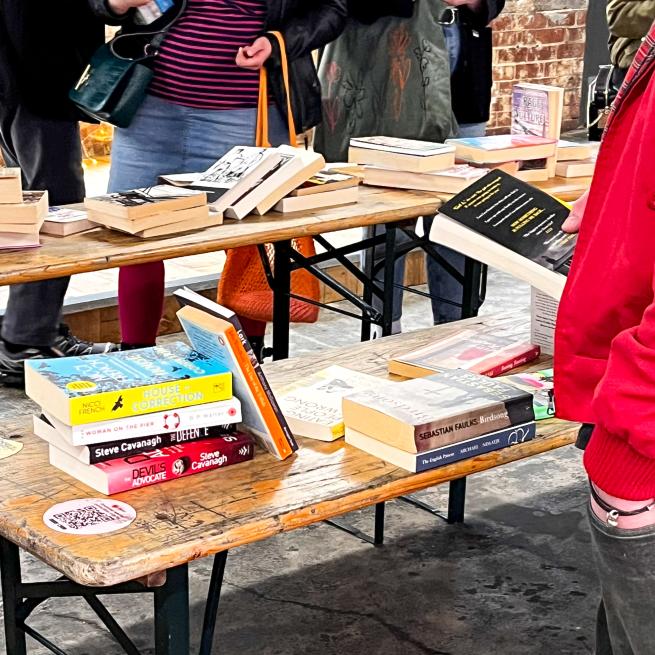 a bench filled with books and people standing around the different books