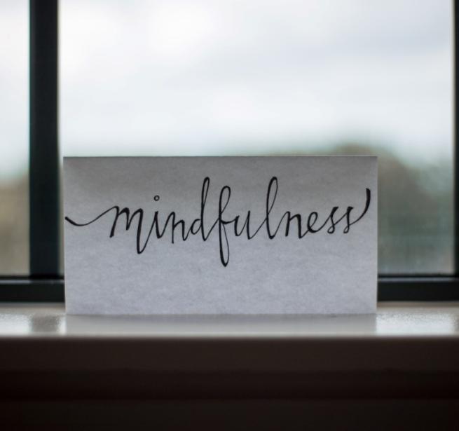 The word "mindfulness" is written on a piece of paper, and stood up on a windowsill against a window