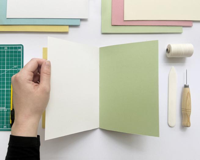 handmade book is opened up on a table with tools surrounding it. 