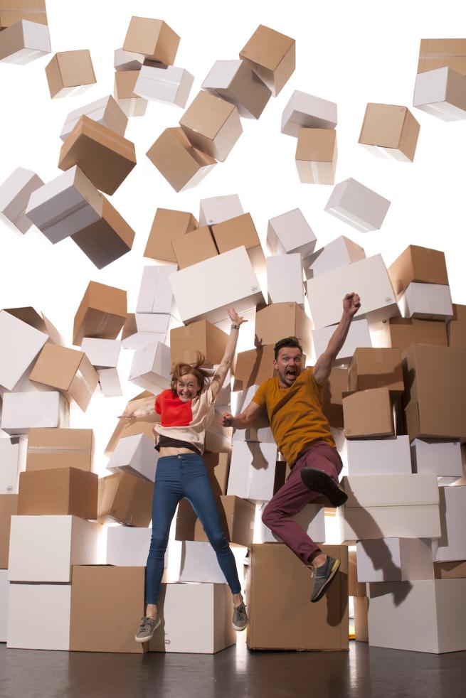 2 people jump in the air in front of carboard boxes