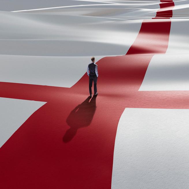 A small figure in a waistcoat stood in the centre of a giant England flag with their back to the camera with their hands in their pockets