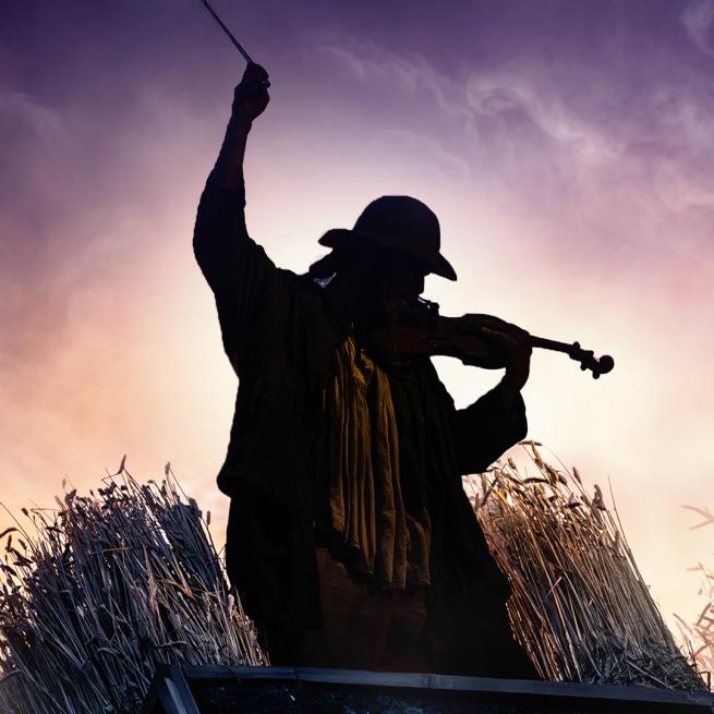 Silhouette of someone in a bowler hat playing a fiddle against some clouds.