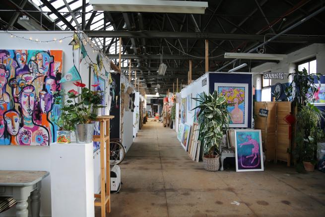 Looking down the length of Spinning Mill Studios with paintings on the walls and plants around. 