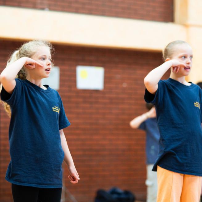 Two children in LHT navy tops in the Leeds Grand Theatre studio holding their hands to their ears as if on the phone