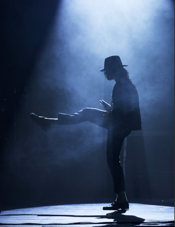 Image of performer in a famous Michael Jackson pose with dramatic lighting around him. 