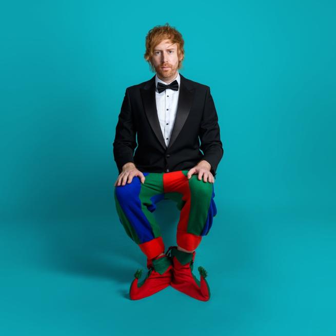 Mark Simmons in a suit, a bow tie and red, blue and green jester trousers.