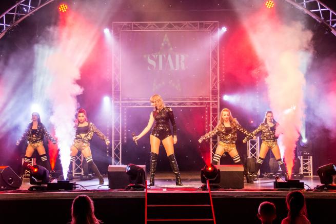 Image of the performer and dancers on stage surrounded by lights. 